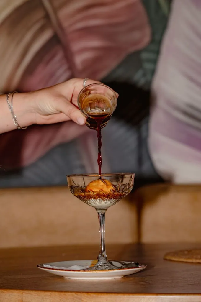 Hete espresso wordt geschonken over een bolletje vanille-ijs in een kristallen glas voor een affogato.