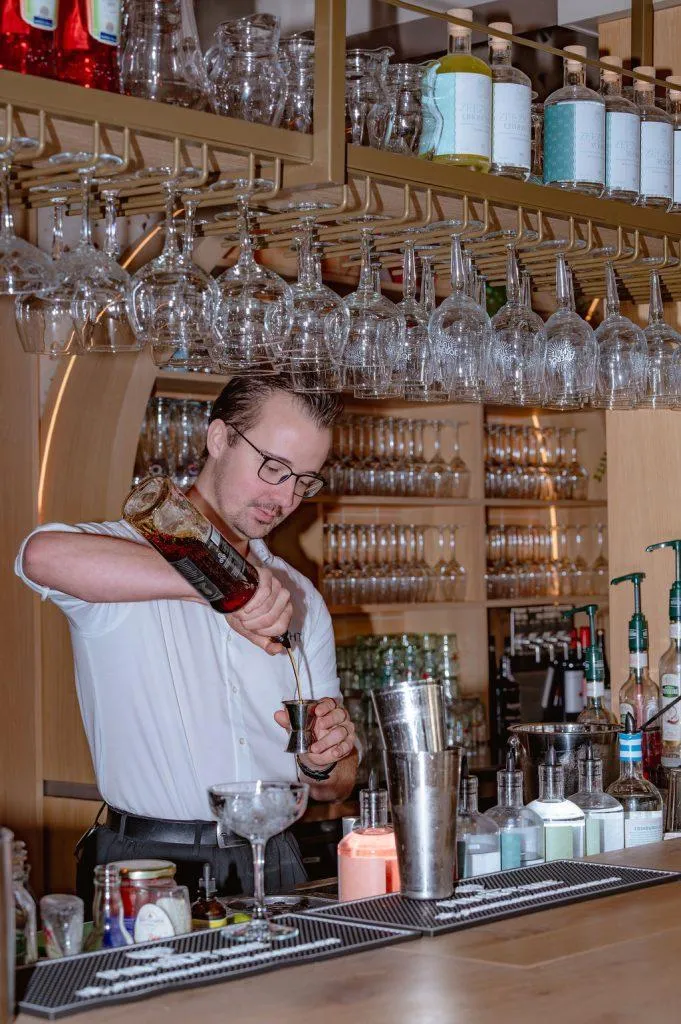 Bartender in wit overhemd schenkt drank in een jigger bij een moderne strandpaviljoen bar met wijnglazen.