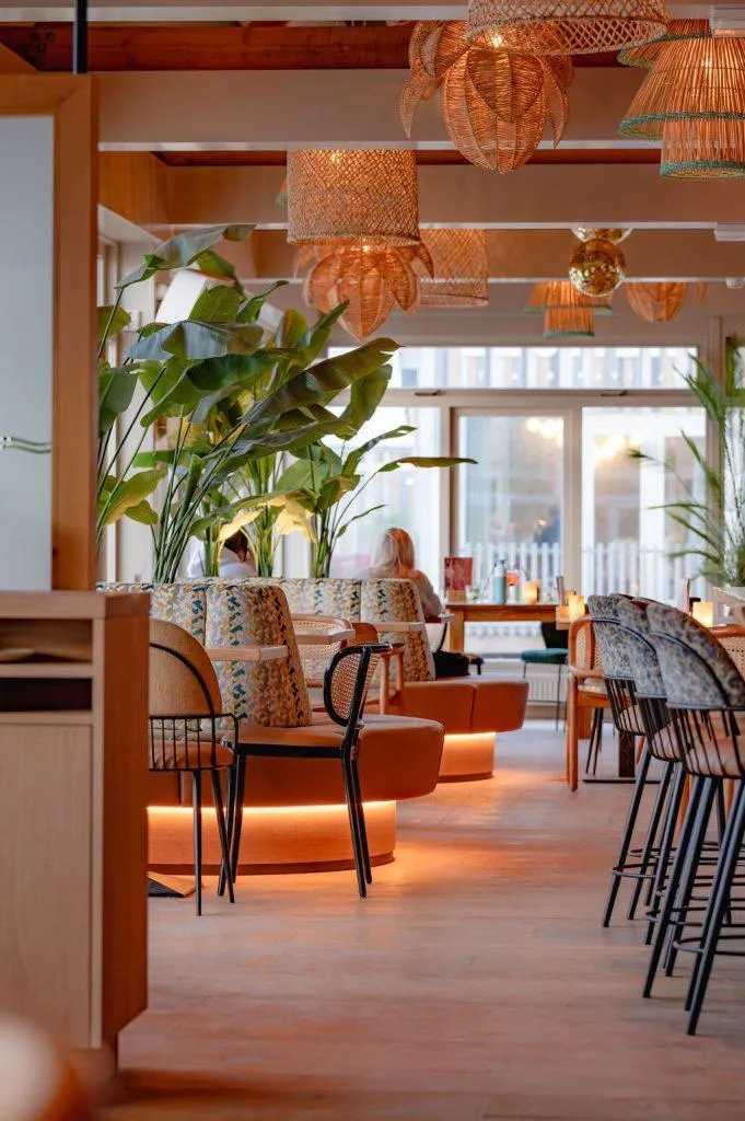 Modern interieur van een strandpaviljoen met rotan lampen, grote groene planten en comfortabele loungebanken.