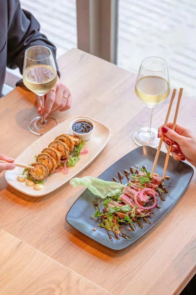 Culinair gedeeld dineren met sushi en geschroeide tonijn geserveerd met witte wijn bij een strandpaviljoen.