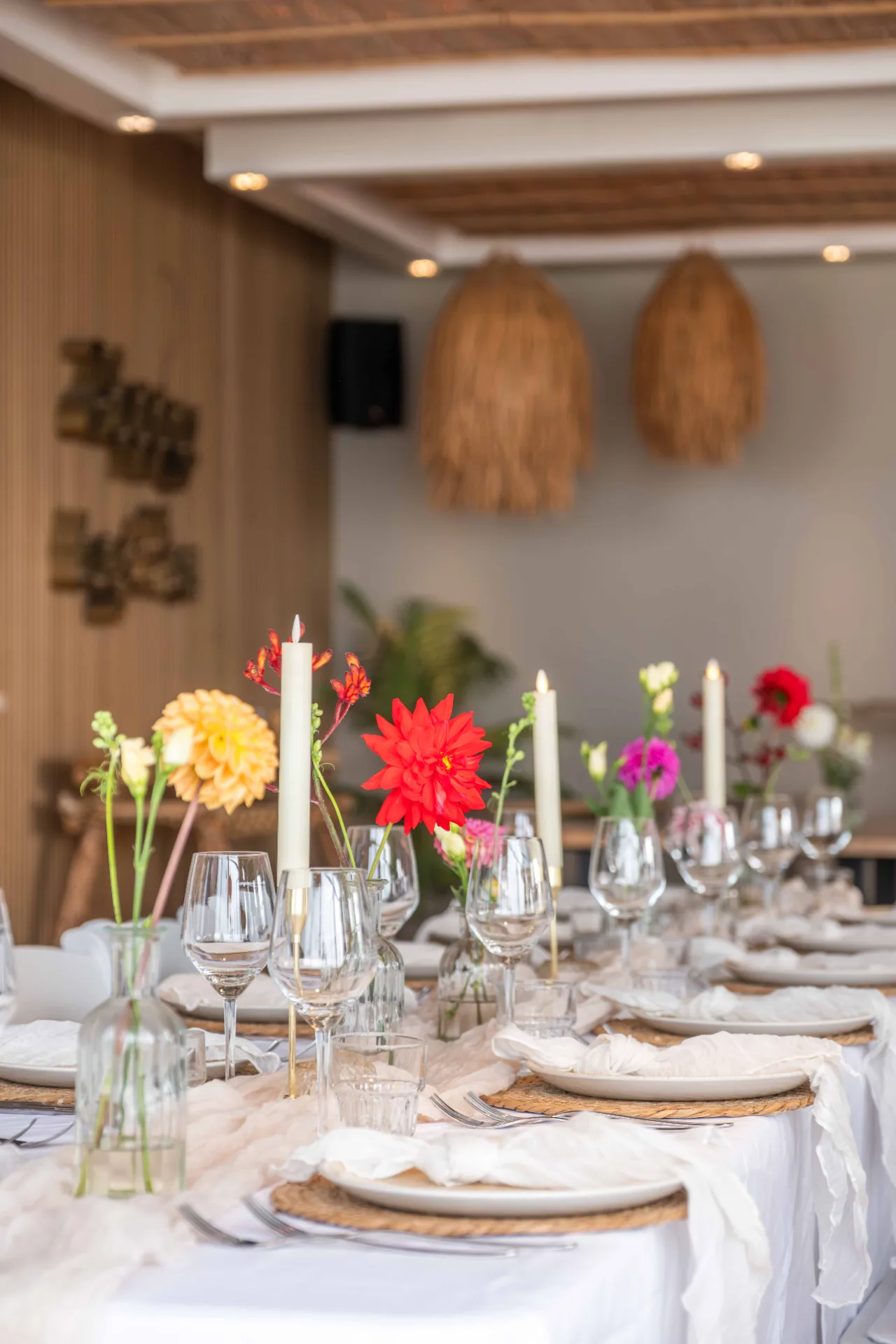 Elegant gedekte dinertafel met kleurrijke bloemen, witte kaarsen en wijnglazen in een strandpaviljoen.