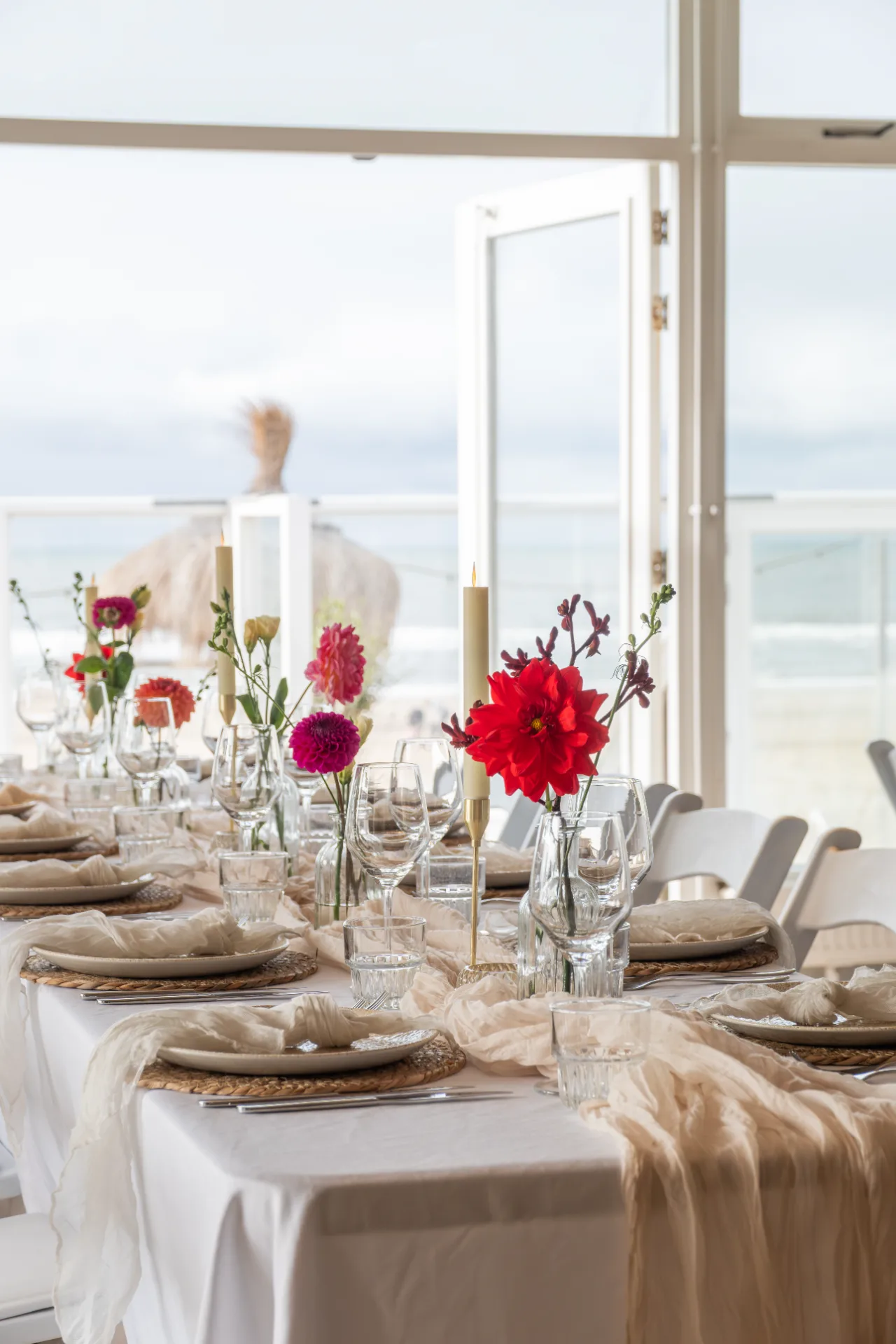 Elegant gedekte tafel met wit linnen, kleurrijke bloemen en kaarsen met uitzicht op zee.