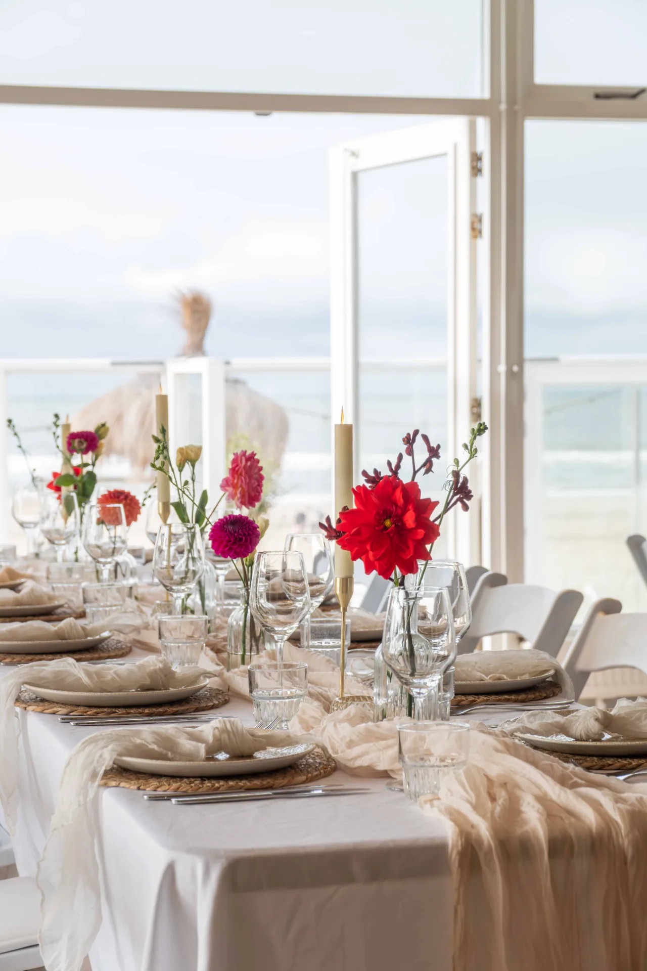 Elegant gedekte tafel met kleurrijke bloemen en kaarsen met uitzicht op het strand en de zee.