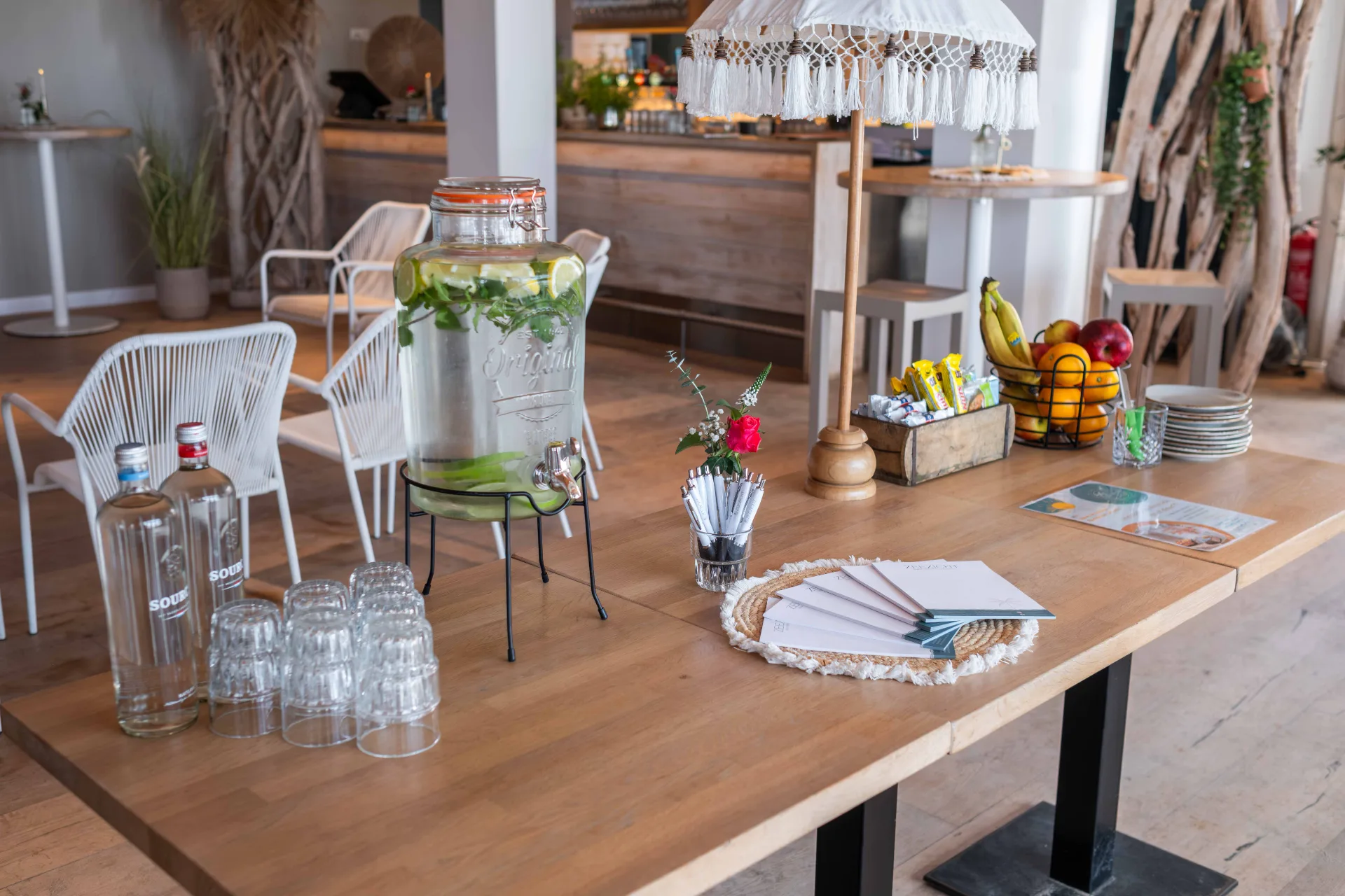 Houten vergadertafel met waterdispenser, vers fruit en notitieblokken in een strandpaviljoen.