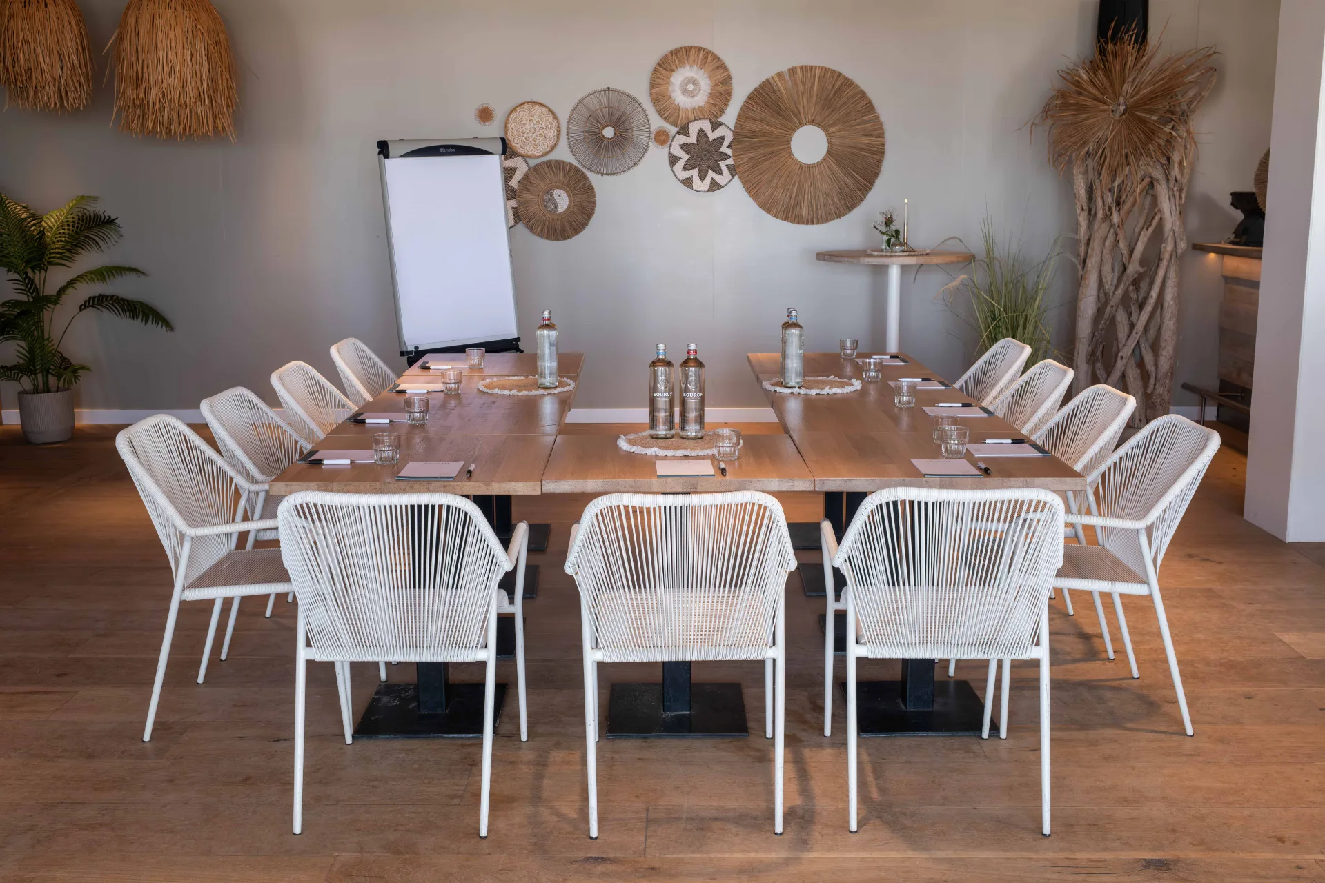 Vergaderopstelling met houten tafels in U-vorm, witte stoelen en flipover in een moderne boho-stijl ruimte.